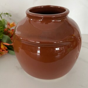 May include: A brown ceramic vase with a rounded shape and a smooth, glossy finish.