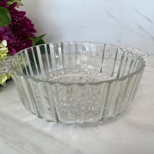 May include: A clear glass bowl with fluted sides and two handles. The bowl has a decorative pattern on the bottom.