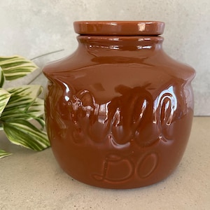 May include: A brown ceramic jar with a lid. The jar has a raised design of the word "Hello" on the front.