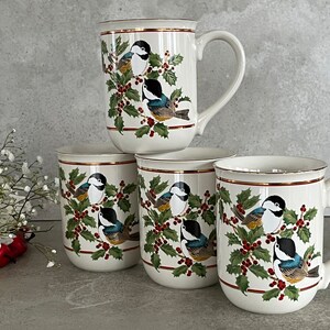 May include: Set of four white ceramic mugs with a gold rim. Each mug features a colorful illustration of birds perched on holly branches with red berries.