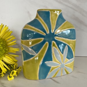 May include: A ceramic vase with a distinctive design. The vase showcases blue and yellow geometric patterns. The vase is approximately 18 cm tall and has a glossy finish. A yellow flower is visible on the left side of the image.