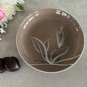 May include: A brown ceramic bowl with a white floral design. The bowl is sitting on a gray surface with two dark chocolate hearts in the foreground.