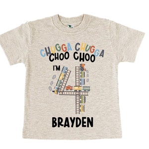 May include: A light grey t-shirt with a colorful train design and the text "Chugga Chugga Choo Choo I'm 4 Brayden".