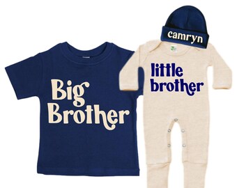 May include: A set of two baby outfits, one navy blue t-shirt with the text "Big Brother" in cream coloured letters and one cream coloured onesie with the text "little brother" in navy blue letters. A navy blue beanie with the name "camryn" in cream coloured letters is also included.