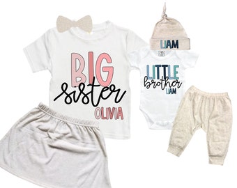 May include: A set of children's clothing, including a white t-shirt with "BIG sister OLIVIA" in pink and black, a skirt, a bow, a onesie with "LITTLE brother LIAM", a hat, and pants. The clothing is in neutral colors.