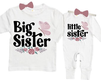 May include: White t-shirt with the text "Big Sister" in black with a pink butterfly and floral design. White long-sleeve onesie with the text "little sister" in black with a pink butterfly and floral design.