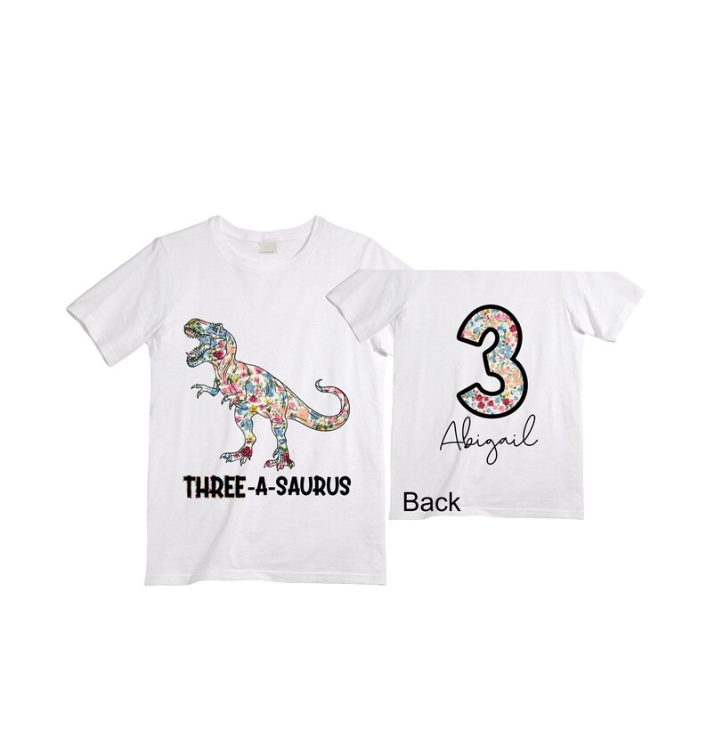 May include: White t-shirt with a floral print dinosaur on the front and the text "THREE-A-SAURUS". The back of the shirt has a floral print number "3" and the name "Abigail".