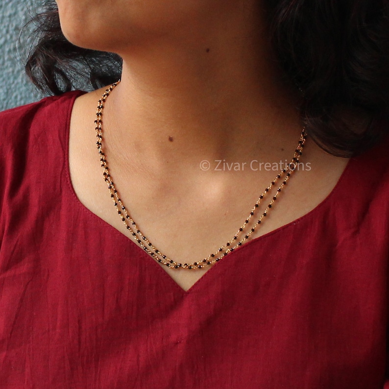 May include: A double-strand necklace with black beads and a gold chain. The necklace is worn by a person with dark hair and a red shirt. &copy; Zivar Creations