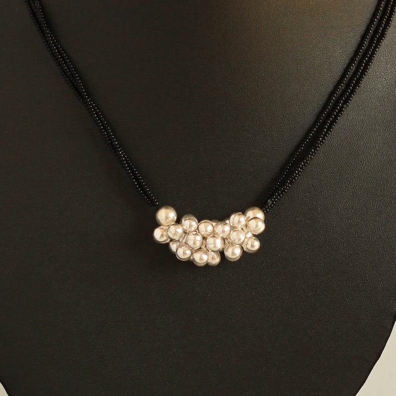 May include: A silver beaded necklace with a cluster of round beads in the center. The necklace is on a black background.