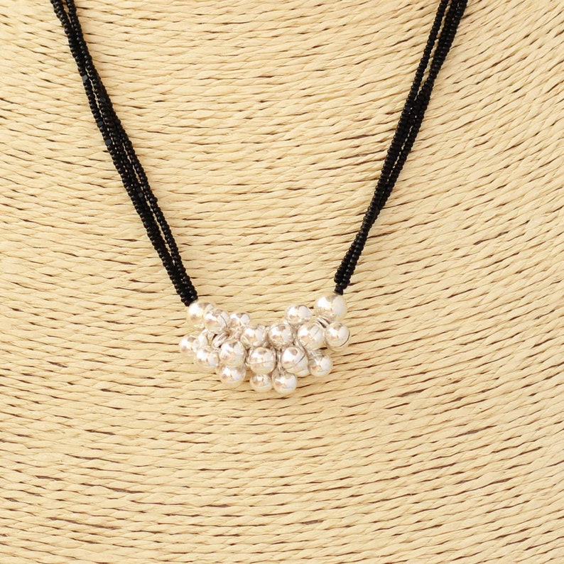 May include: A black beaded necklace with a silver charm pendant. The charm is a cluster of small, round silver beads.