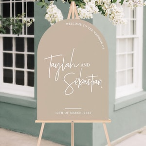 May include: A light brown arch-shaped welcome sign with white text that reads "Welcome to the Wedding of Taylah and Sebastian 12th of March, 2025".