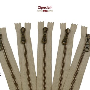Könnte beinhalten: Fünf beigefarbene Metallreißverschlüsse mit antiken Messing-Zierbändern. Die Reißverschlüsse sind 572 beige.