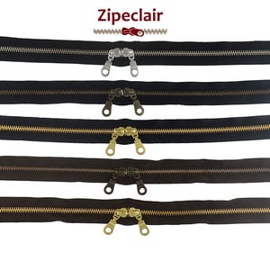May include: Five horizontal zipper strips with the text Zipeclair at the top. The zippers feature black or dark brown fabric tape with metal teeth and double sliders in silver, antique brass, gold, and bronze finishes, arranged in a vertical row.