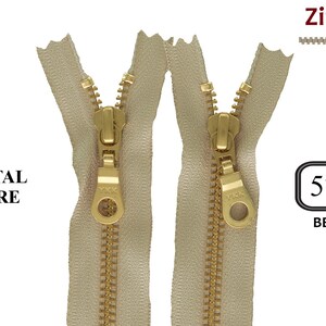 Op de afbeelding: Twee beige ritsen met gouden metalen tanden en schuifjes. De ritsen zijn gelabeld "572 Beige" en "Metal Dore".
