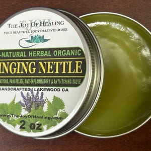 May include: A round, silver tin of Stinging Nettle salve, with the lid partially open. The label reads "The Joy of Healing" and lists the product as all-natural and organic. The salve is 2 oz.