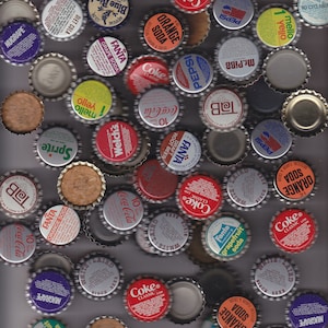 Peut inclure: Une collection de capsules de bouteilles vintage de différentes marques de sodas, notamment Coca-Cola, Pepsi, Sprite, Fanta et Welch's. Les capsules sont d'un mélange de couleurs, notamment rouge, bleu, vert, jaune et blanc.