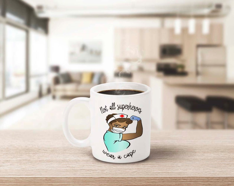 Peut inclure: Mug en c&eacute;ramique blanche avec une anse, remplie de caf&eacute; noir. La tasse pr&eacute;sente une illustration de dessin anim&eacute; d'une infirmi&egrave;re fl&eacute;chissant son bras, avec le texte "Not all superheroes wear a cape."