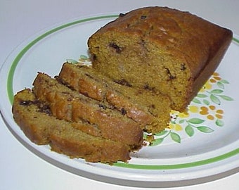 May include: A plate of sliced pumpkin bread with chocolate chips. The bread is golden brown and has a slightly crispy crust. The plate has a floral design with green leaves and orange flowers.