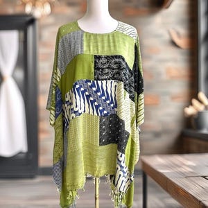 May include: A loose-fitting tunic featuring a patchwork design of lime green, black, and blue fabric panels with various intricate patterns. The garment has a round neckline, short sleeves, and a hemline finished with decorative fringe tassels.
