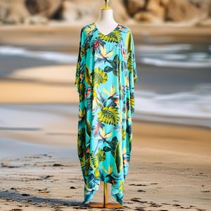 May include: A loose-fitting, floor-length kaftan dress featuring a vibrant turquoise base color with a repeating tropical print of large green monstera leaves and orange bird of paradise flowers, designed with a V-neckline and wide sleeves.