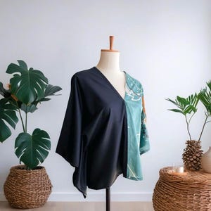 May include: A two-toned kimono-style top. One side is solid black, the other is a teal and white patterned design. The top has a V-neck and wide sleeves. It is displayed on a mannequin.