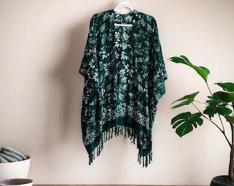 May include: A dark green kimono-style wrap featuring a white botanical leaf pattern throughout. The garment has an open front, wide sleeves, and a hemline finished with long, matching green fringe tassels along the bottom edge.