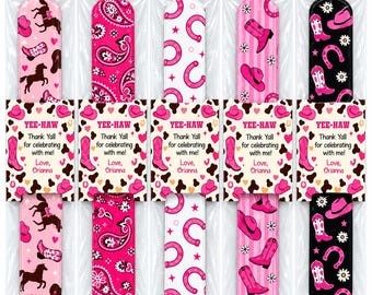 May include: Five slap bracelets in clear plastic packaging, each featuring distinct pink, white, and black western-themed patterns including horses, paisley, horseshoes, and cowboy boots. Each bracelet has a tag reading YEE-HAW Thank Yall for celebrating with me! Love, Orianna.