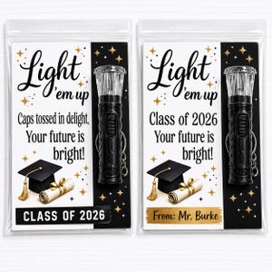 May include: Two clear plastic bags containing black flashlights with keychains attached to cards. The cards feature the text Light 'em up, graduation cap and diploma illustrations, gold stars, and the text Class of 2026 and From: Mr. Burke.