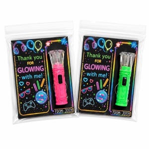 May include: Two clear plastic bags containing a small flashlight attached to a black card. The card features neon-colored graphics of headphones, balloons, hearts, glasses, and a game controller with the text Thank you FOR GLOWING with me! FROM: JOSH.