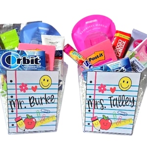 May include: Two gift baskets filled with various items, including Orbit gum, face masks, and Post-it notes. Each basket has a notepad design with a smiling face, apple, pencil, and the names "Mr. Burke" and "Mrs. Talley."