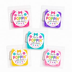 May include: Five square silicone fidget toys in pink, purple, teal, yellow, and light pink, each with a metal ball chain and a circular sticker reading You're POPPIN' with cheer! From: Coach Kelly, featuring a bow and colorful bunting.
