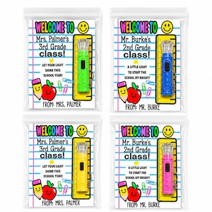 May include: Four clear plastic bags containing school-themed gift cards with attached mini flashlights. The cards feature text like Welcome to Mrs. Palmer's 3rd Grade class or Mr. Burke's 2nd Grade class, alongside illustrations of a pencil, apple, and ruler.