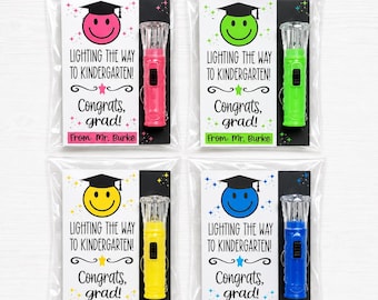 May include: Four cellophane-wrapped gifts. Each includes a colorful flashlight and a card with a smiley face wearing a graduation cap. The cards read "Lighting the Way to Kindergarten! Congrats, grad!" and "From: Mr. Burke."