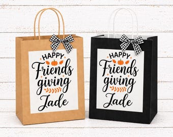 以下が含まれることがあります： 茶色と黒の紙製ギフトバッグ2枚。それぞれに「HAPPY Friends giving Jade」という黒い文字とオレンジ色のカボチャと葉のグラフィックが描かれた白い長方形のラベルが貼られ、黒と白のギンガムチェックのリボンが結ばれています。