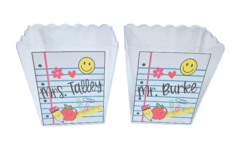 May include: Two white, scalloped-edge containers with notebook paper designs. Each features a smiley face, hearts, flowers, and school-themed graphics. One reads "Mrs. Talley" and the other "Mr. Burke".