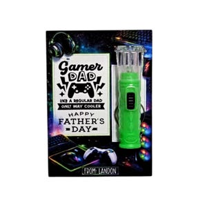 Pu&ograve; includere: Un biglietto per la festa del pap&agrave; a tema gaming. Il biglietto presenta il testo "Gamer Dad" e una grafica del controller. Un gadget verde illuminato &egrave; sulla destra. Il biglietto &egrave; decorato con accessori di gioco e il testo "From: Landon."