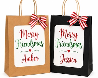 May include: Two gift bags, one brown and one black, each featuring a white rectangular label with the red and green text Merry Friendsmas, a small red heart, and a name, Amber or Jessica, topped with a red and white striped fabric bow.