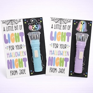 Puede incluir: Dos tarjetas de regalo con temática de Halloween con linternas. Una tarjeta tiene un sombrero de bruja y una linterna azul, la otra tiene un fantasma y una linterna morada. Las tarjetas dicen: "Un poco de luz para tu noche de Halloween de: Jade."
