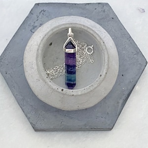 May include: A silver chain necklace with a purple, green and blue fluorite crystal pendant. The pendant is shaped like a point and has a silver cap on the top.