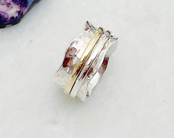 Pode incluir: Um anel giratório de prata e ouro com um design texturizado e ondulado. O anel é feito de duas bandas de prata com uma banda de ouro no meio.