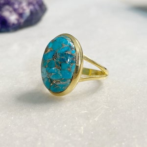May include: A gold ring with a large oval turquoise stone. The stone is a mosaic of smaller turquoise pieces.