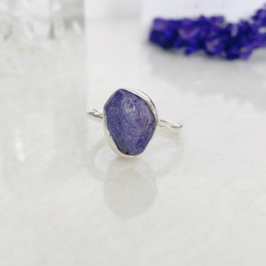 May include: A silver ring featuring a raw, purple amethyst gemstone set in a bezel setting.