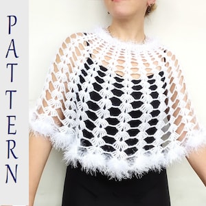Puede incluir: Poncho de crochet blanco con un diseño de encaje y un ribete blanco esponjoso. El poncho se lleva sobre una blusa negra.