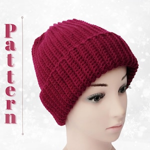 May include: A close-up of a burgundy crocheted beanie hat. The hat is made with a ribbed stitch and has a folded brim.