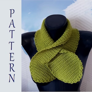 May include: A green crocheted infinity scarf with a unique knotted design. The scarf is displayed on a black mannequin.