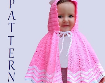 Puede incluir: Una capa con capucha de ganchillo rosa con ribetes blancos, puesta por un niño. La capa tiene un delicado patrón de encaje y un lazo blanco en el cuello.