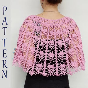 Pode incluir: Um xale de crochê rosa com um delicado padrão de renda. O xale está drapeado sobre os ombros de uma pessoa e tem uma borda festonada.
