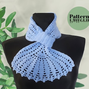 May include: A light blue crocheted scarf with a delicate, lacy pattern. The scarf is tied in a knot around a black mannequin's neck. The text "Pattern Butterfly" is visible in a green circle in the upper right corner of the image.