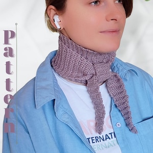 Op de afbeelding: Een lavendelkleurige, gehaakte nekwarmer met lange, puntige uiteinden. De nekwarmer wordt gedragen over een wit T-shirt en een lichtblauw spijkeroverhemd. Het woord "Pattern" is zichtbaar aan de linkerkant van de afbeelding.