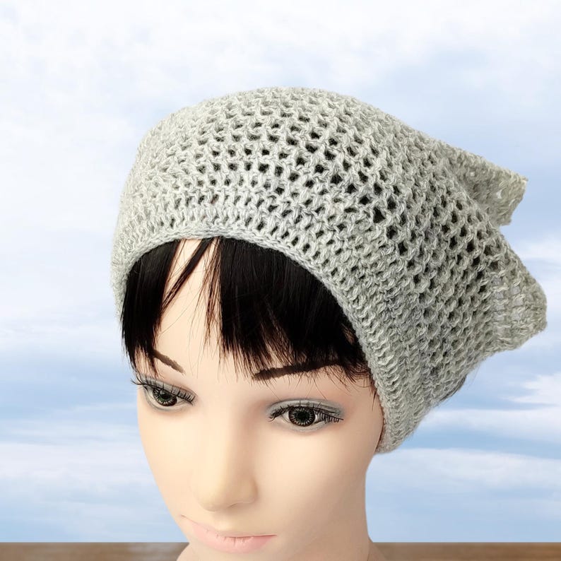 Peut inclure: Un b&eacute;ret gris en crochet avec une maille l&acirc;che et ouverte. Le b&eacute;ret est port&eacute; sur une t&ecirc;te de mannequin avec des cheveux noirs courts.